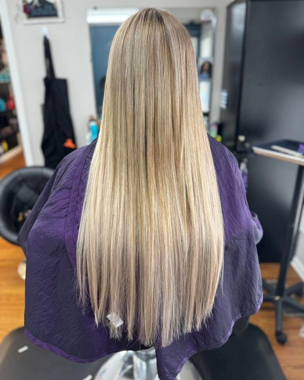 Long straight blonde hair with subtle highlights, viewed from behind in a salon chair.