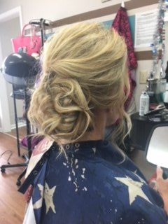 Blonde updo hairstyle in a salon chair, with loose curls pinned at the nape of the neck.