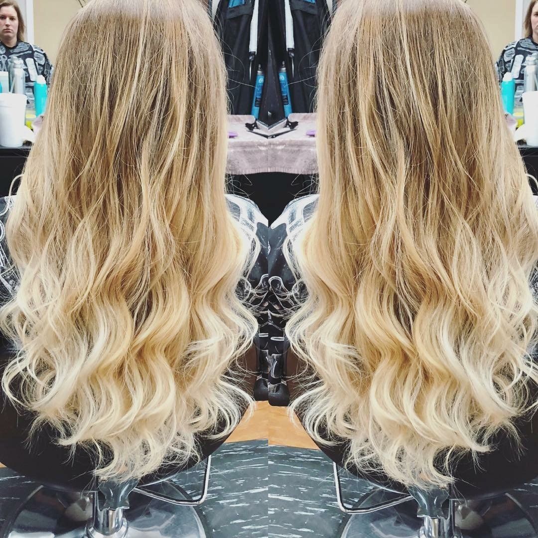 Side-by-side view of long wavy blonde hair with dark roots, shown from the back in a salon mirror.