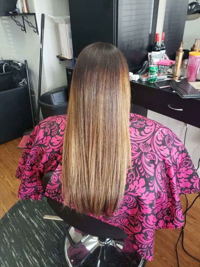 Person with long straight hair sits at a desk, wearing a pink patterned cape in a salon.