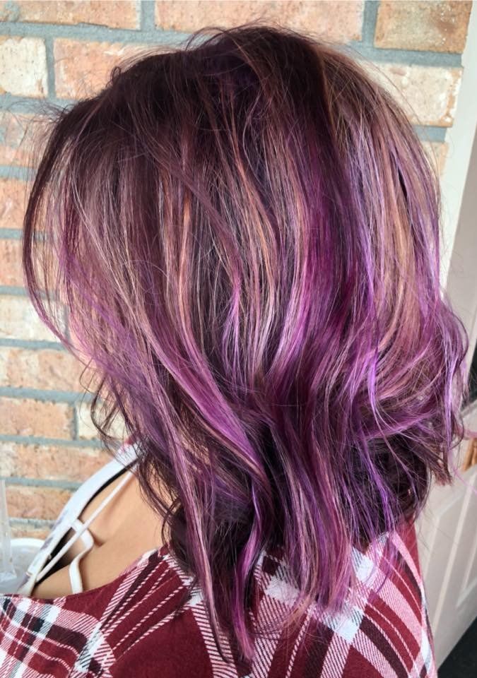 Side view of shoulder-length wavy hair dyed burgundy and purple against a brick wall