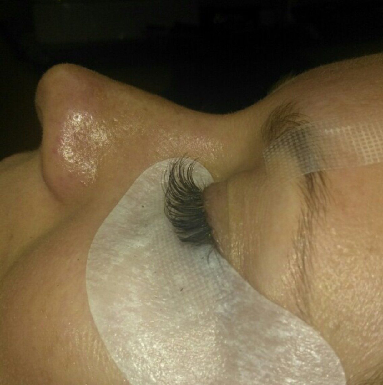 Close-up of a person’s closed eye with a white under-eye eye pad applied, showing a long eyelash extension.