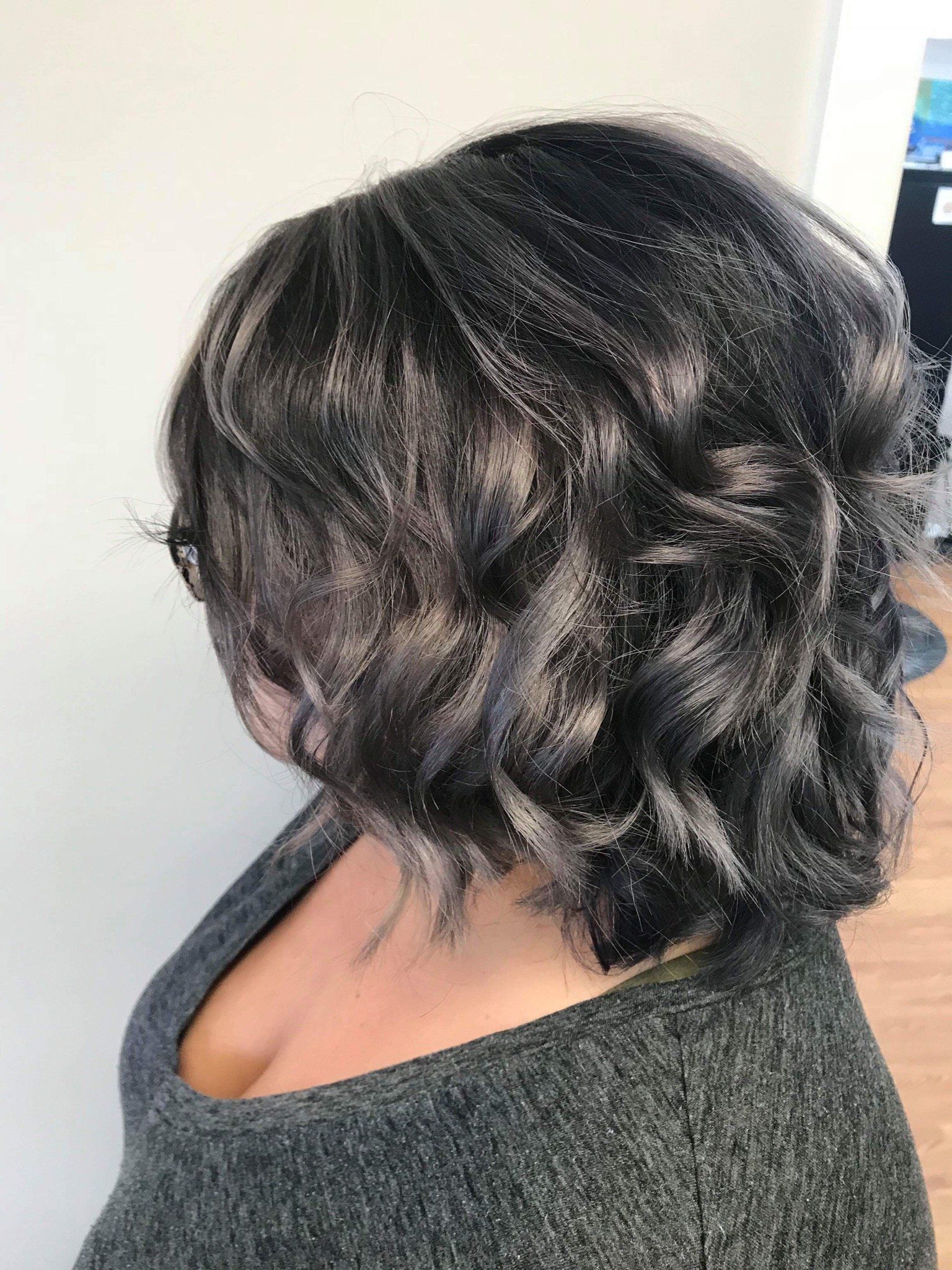 Short dark wavy hairstyle with loose curls, shown in profile against a plain light background