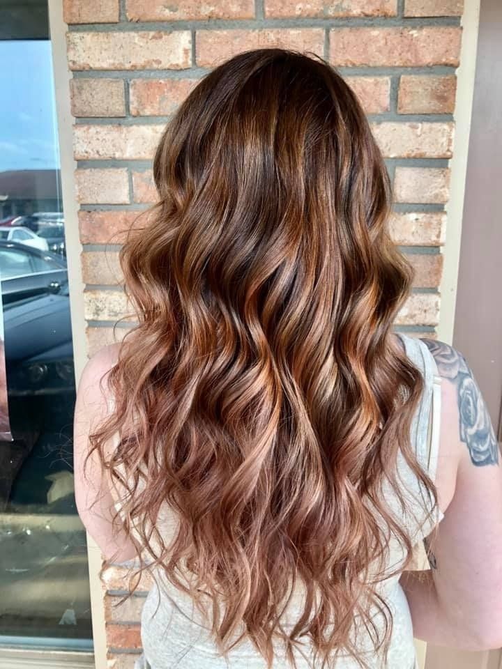 Long wavy brown hair with caramel highlights, seen from behind against a brick wall.
