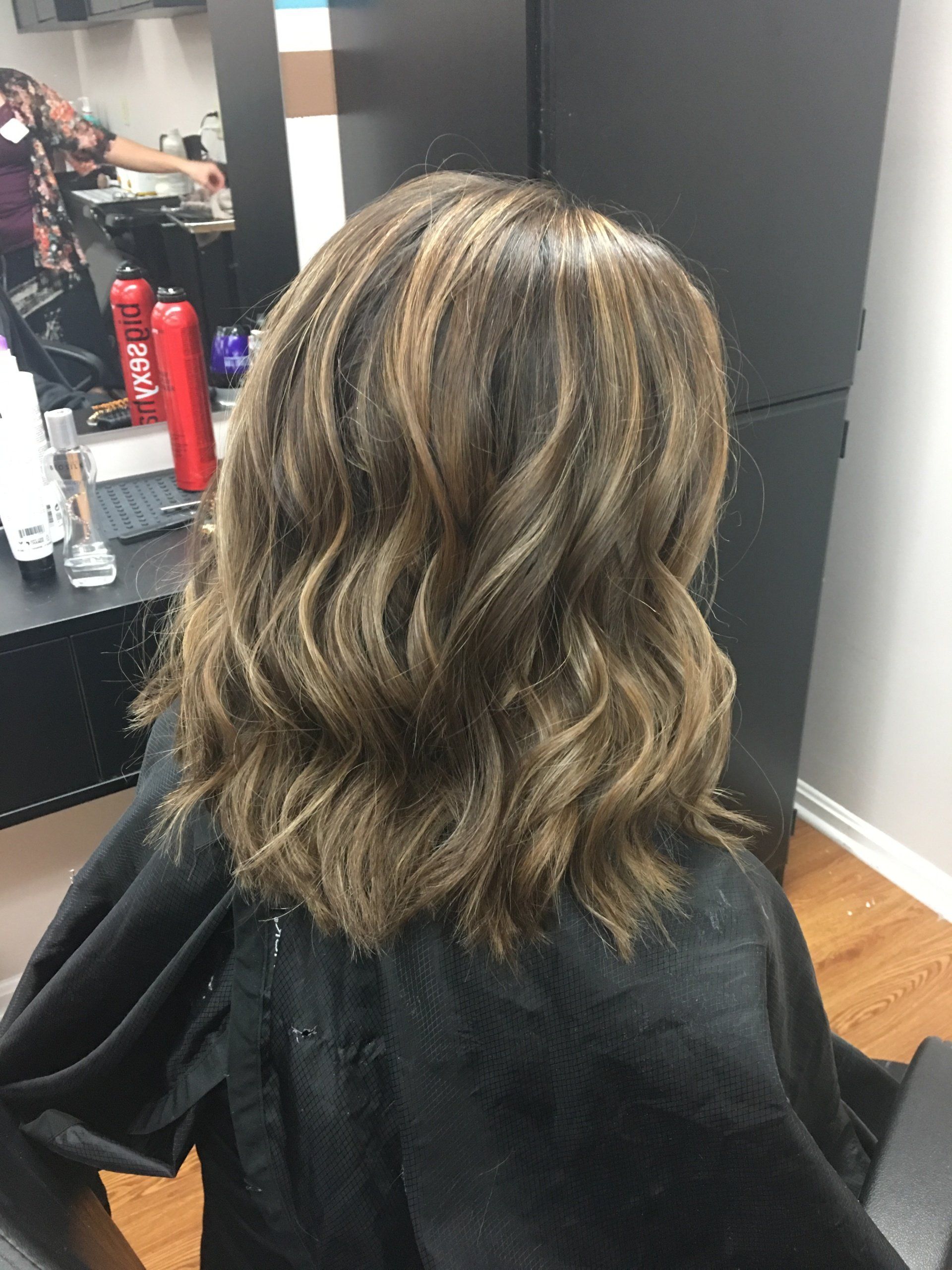 Wavy shoulder-length hair with blonde highlights in a salon chair, viewed from behind.