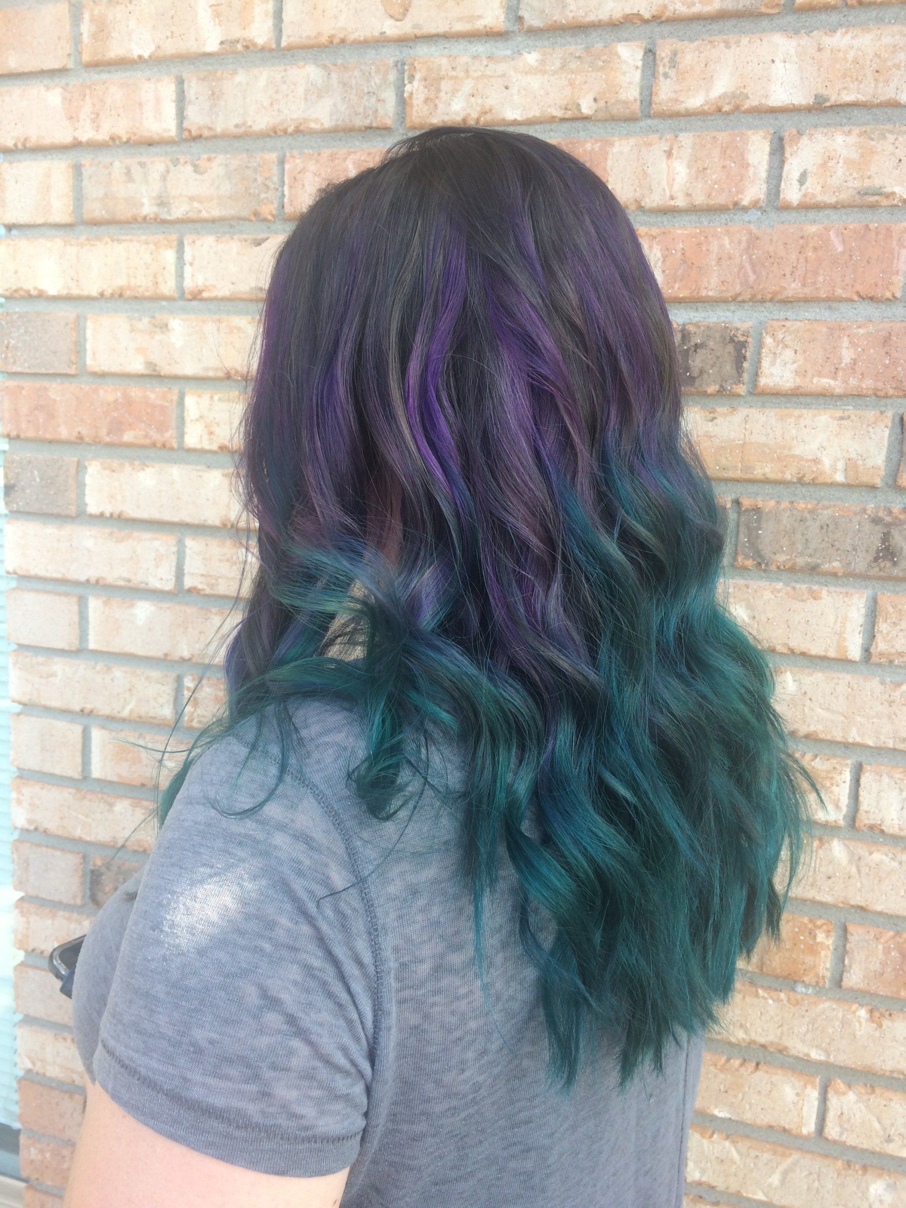 Person with purple-to-teal ombré hair seen from behind against a brick wall