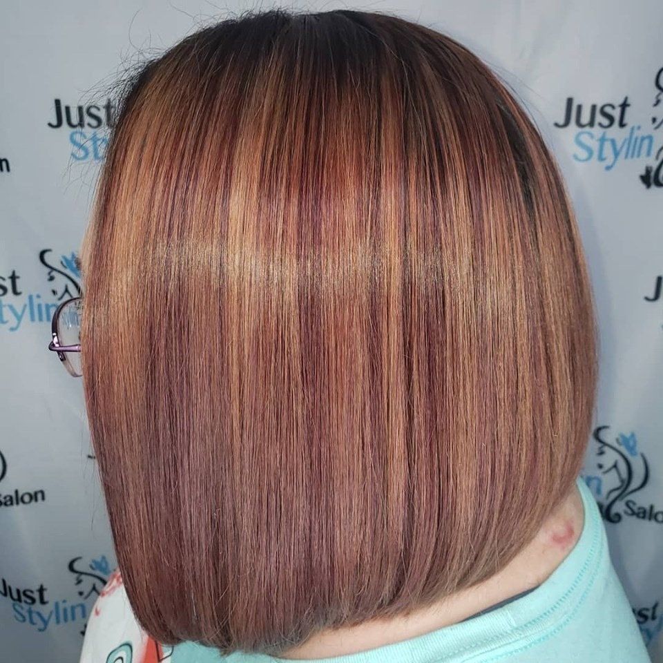 Short layered bob haircut with copper highlights, shown from the back against a salon backdrop