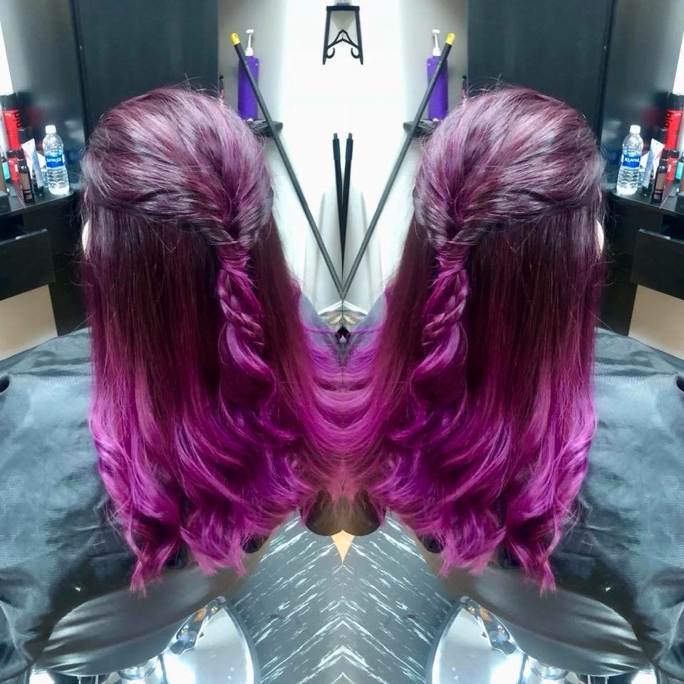 Mirrored view of a person’s wavy magenta hair in a salon chair, with dark burgundy roots.