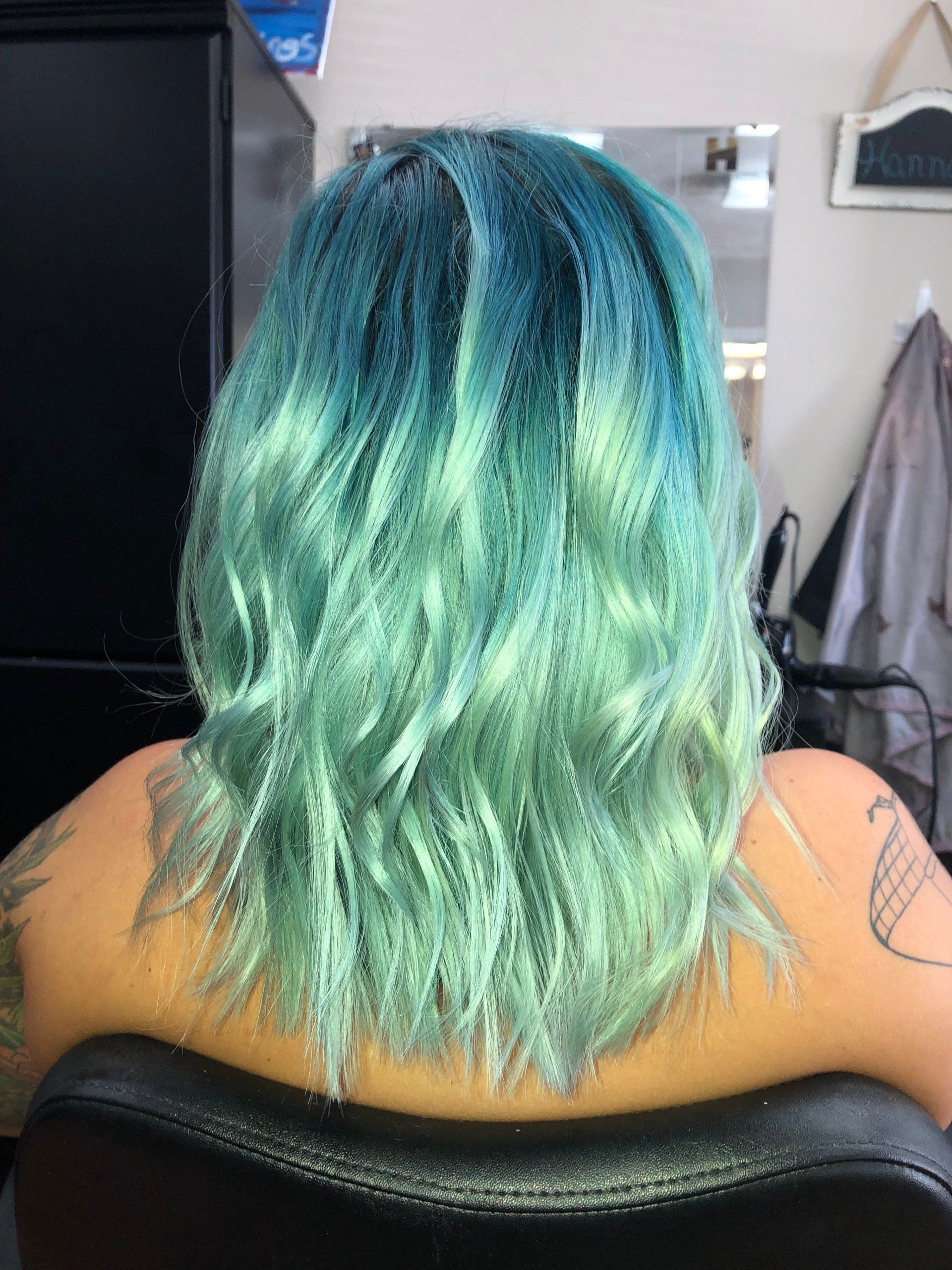 Person with teal-to-green wavy hair seen from behind in a salon chair.