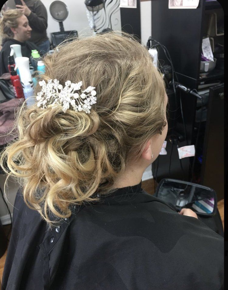 Curly blonde updo with white flowers, seen from behind in a salon chair