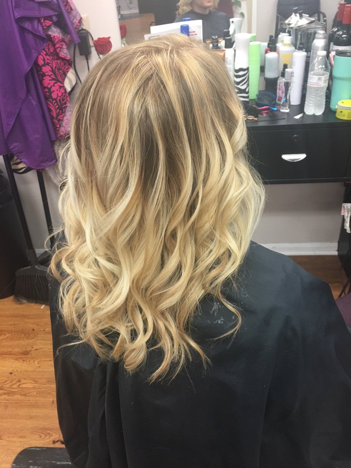 Wavy blonde hair styled in loose curls from the back in a salon chair