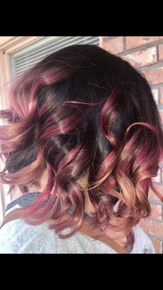Short curly burgundy hair with pink highlights, viewed from the back against a brick wall.
