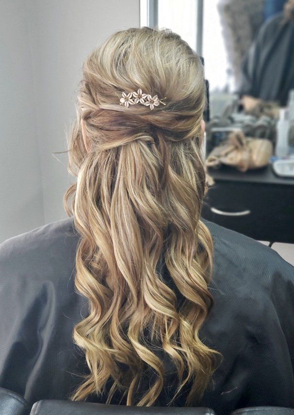 Long blonde wavy half-up hairstyle with a jeweled hair clip, shown from the back in a salon.