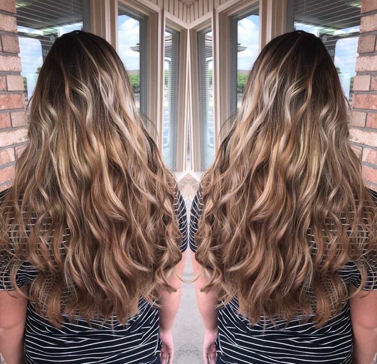 Mirrored view of long wavy brown hair from behind in a bright brick-lined walkway