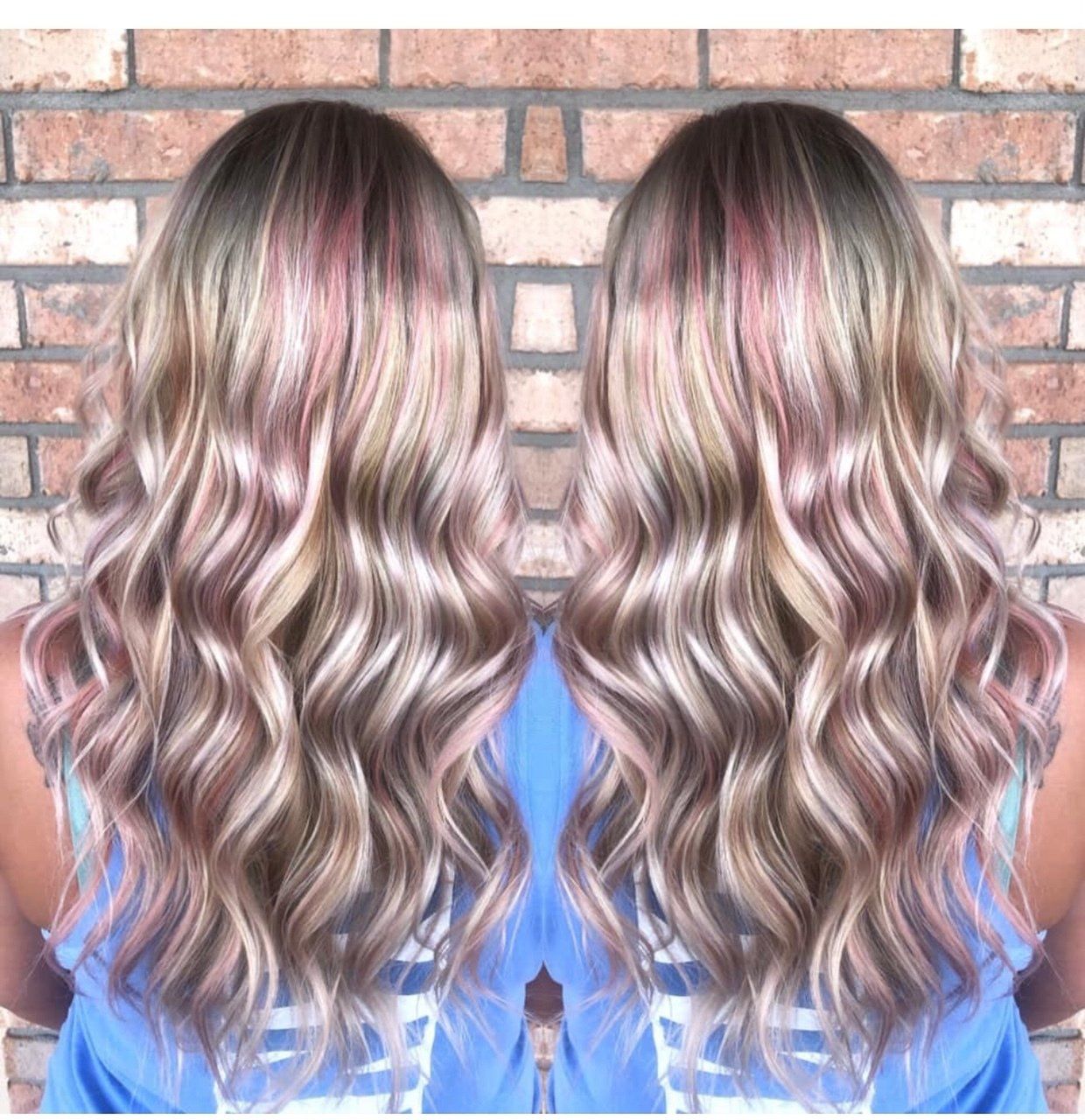 Back view of long, wavy blonde hair with pink highlights against a brick wall