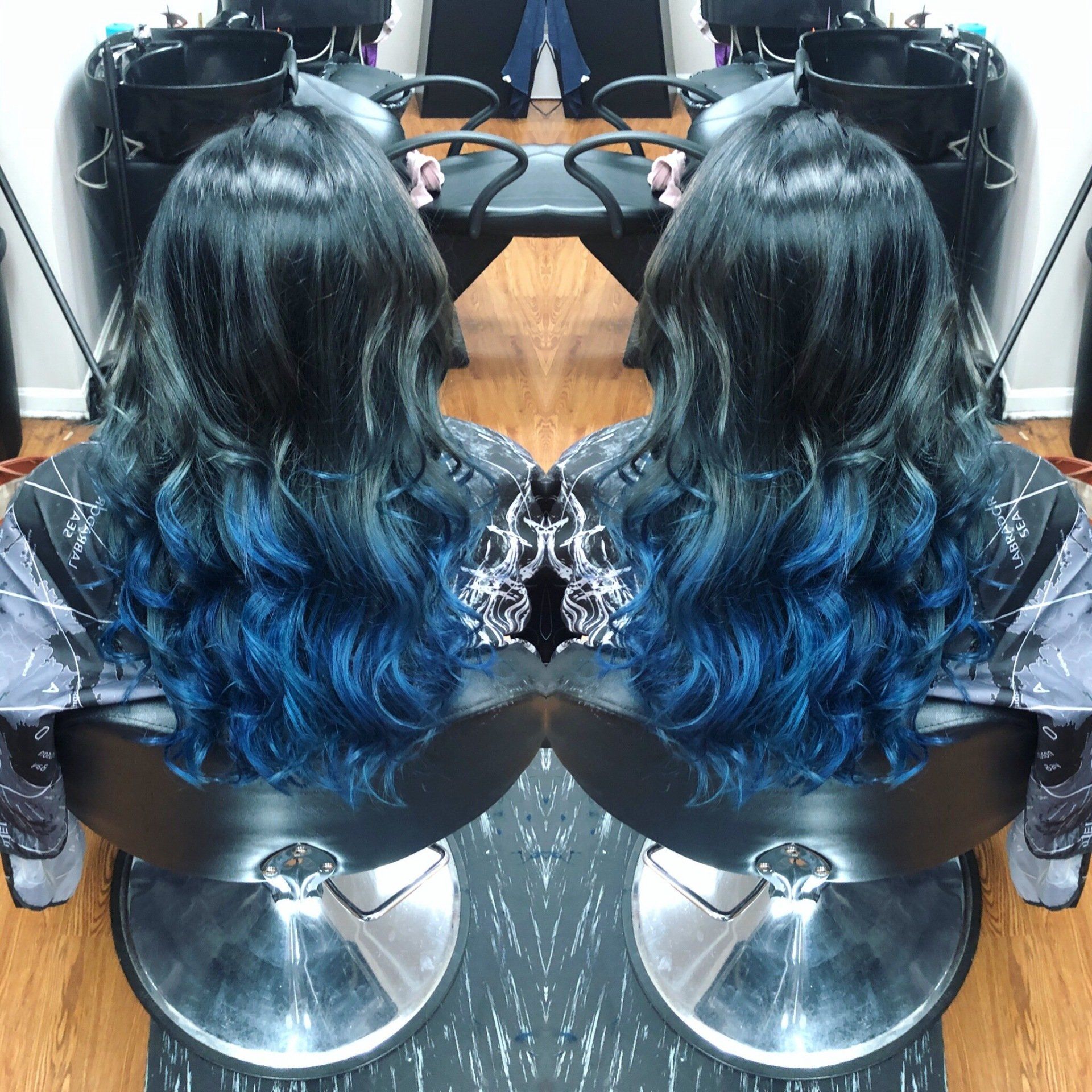 Salon chair with long wavy black hair dyed blue at the ends, shown in a mirrored view
