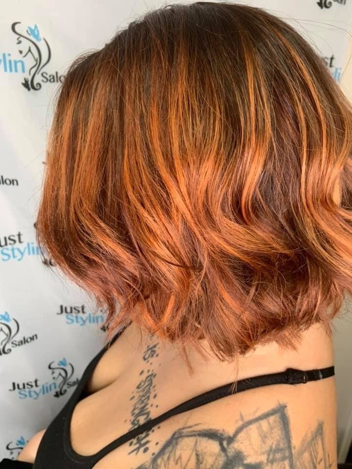 Side-view short wavy copper bob with dark roots, showing a tattooed shoulder.