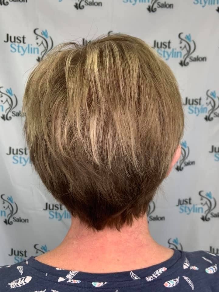 Short blonde layered haircut shown from the back against a salon-branded backdrop