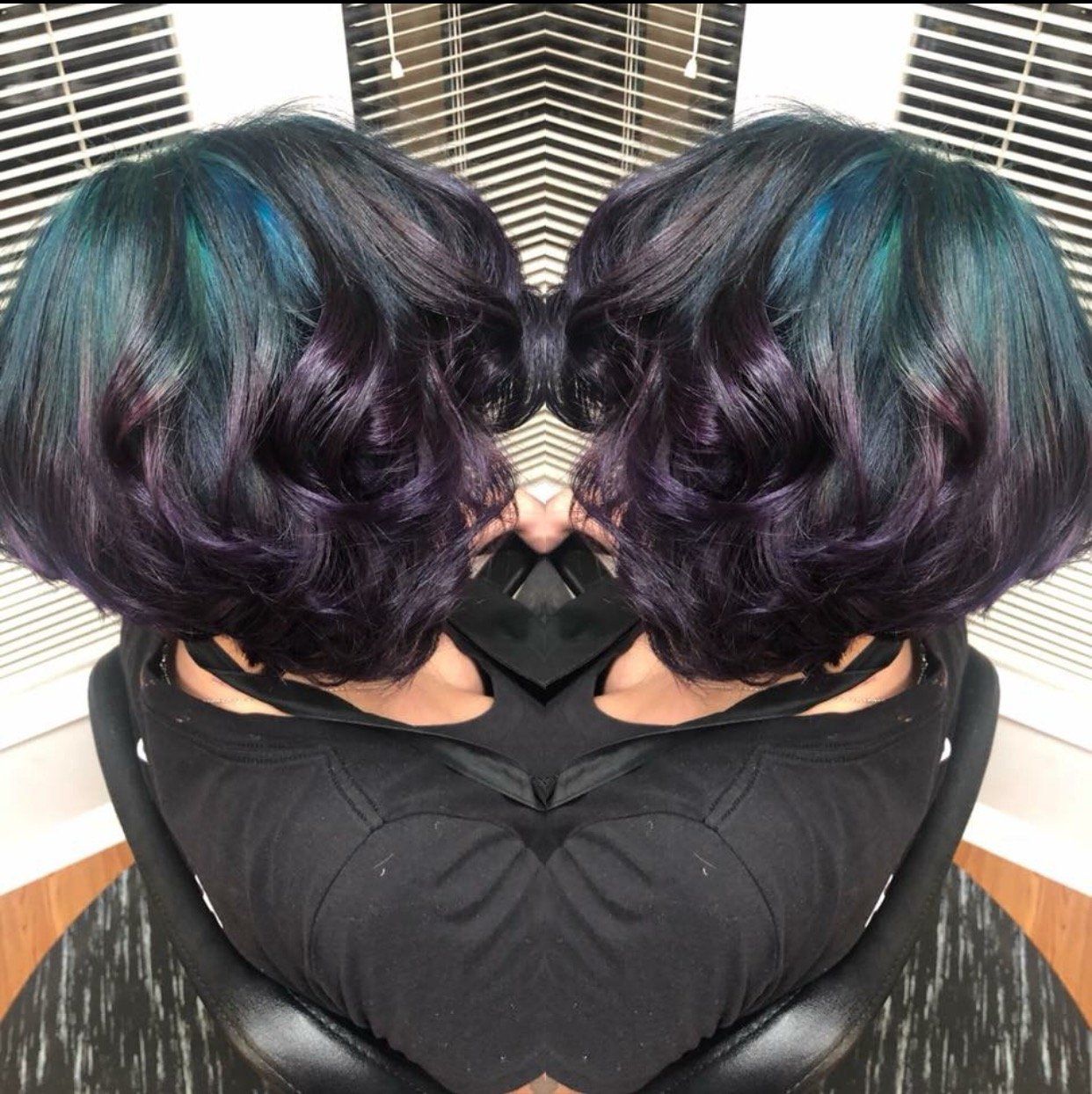 Mirrored photo of a short wavy purple-and-teal hairstyle in a salon chair
