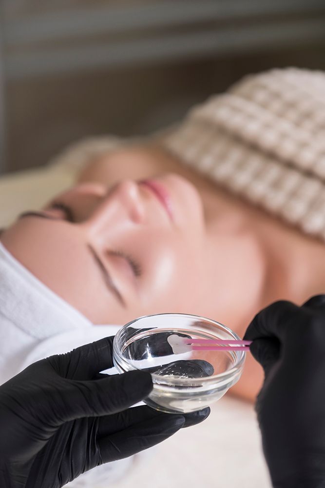 Gloved hands holding a glass cup over a person lying face down during a spa facial treatment