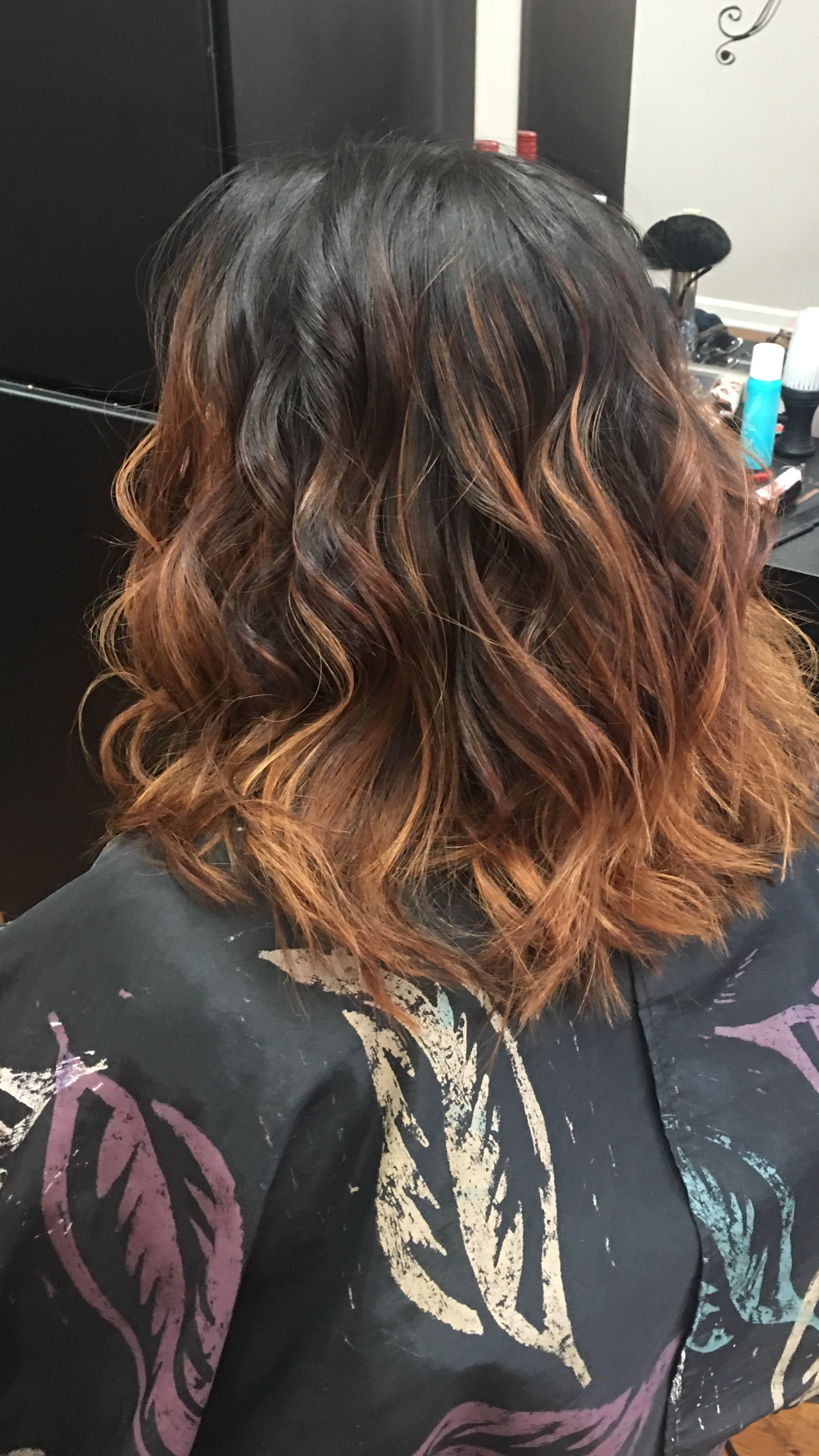 Back view of shoulder-length wavy black hair with copper highlights, wearing a black patterned shirt.
