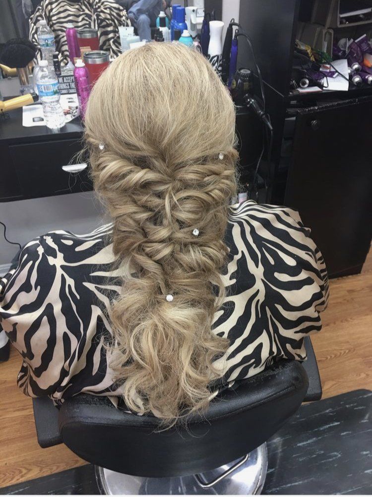 Blonde hair styled in a loose braided half-updo with curled ends, shown from the back in a salon chair.
