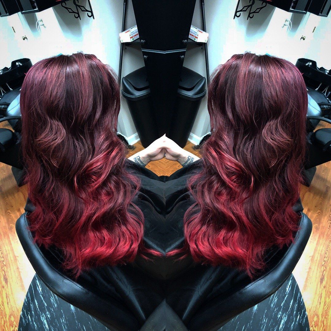 Mirrored view of a salon chair with long wavy burgundy hair cascading down the back
