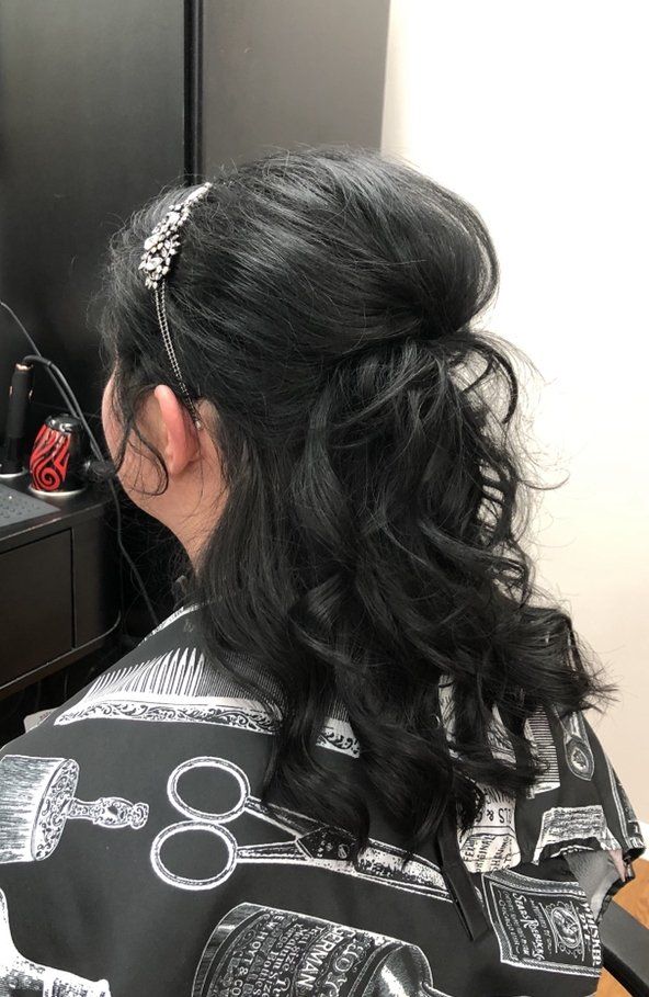 Woman with dark wavy half-up hairstyle and silver hair clip, seen from behind in a salon chair.