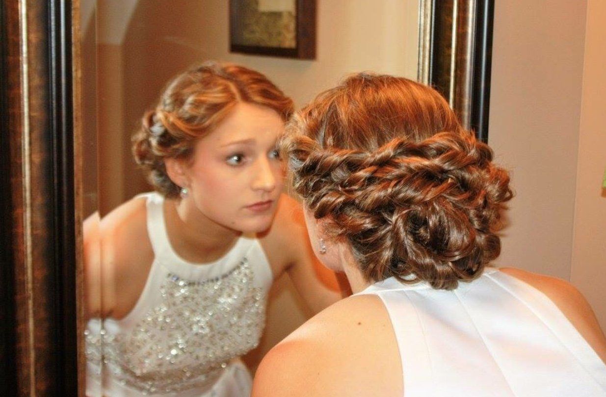 Woman in a white dress looking into a mirror while adjusting her hair in a warmly lit room