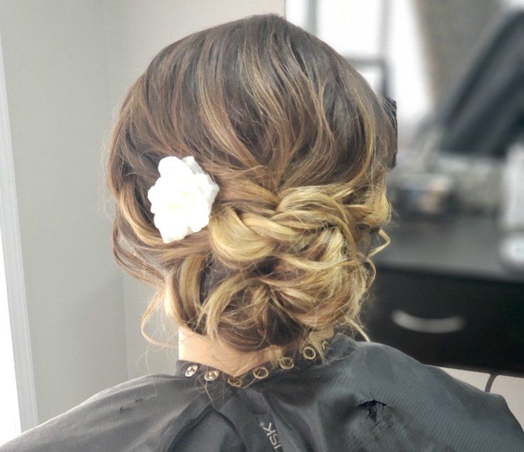 Braided updo hairstyle with soft waves and a white flower accessory, viewed from the back
