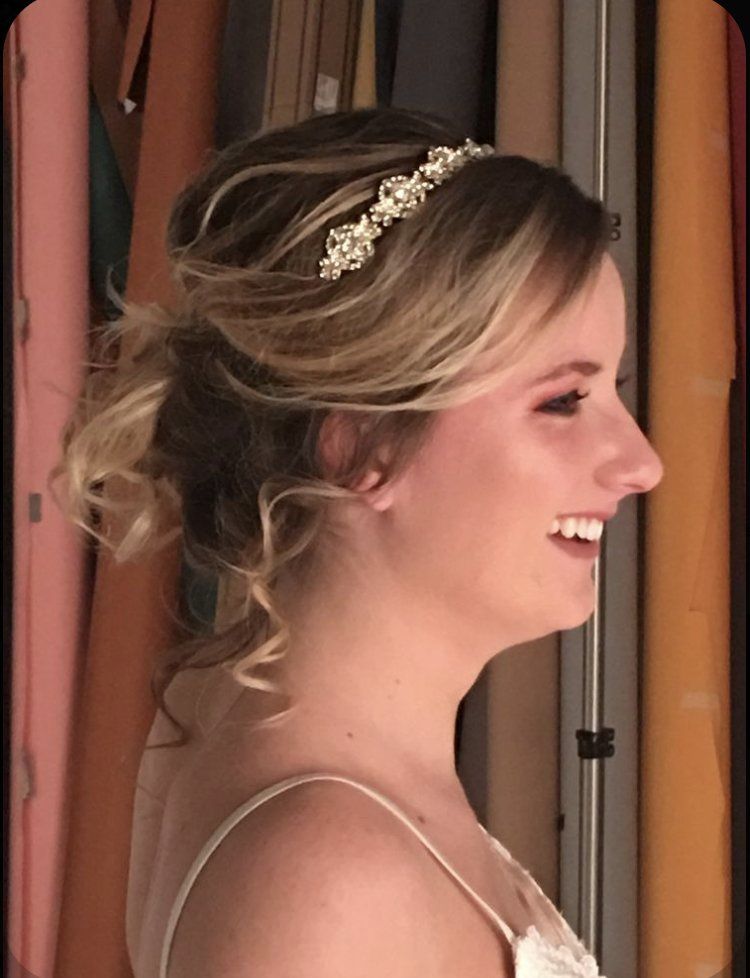 Profile view of a smiling woman with an elegant updo and jeweled headband, wearing a spaghetti-strap dress.