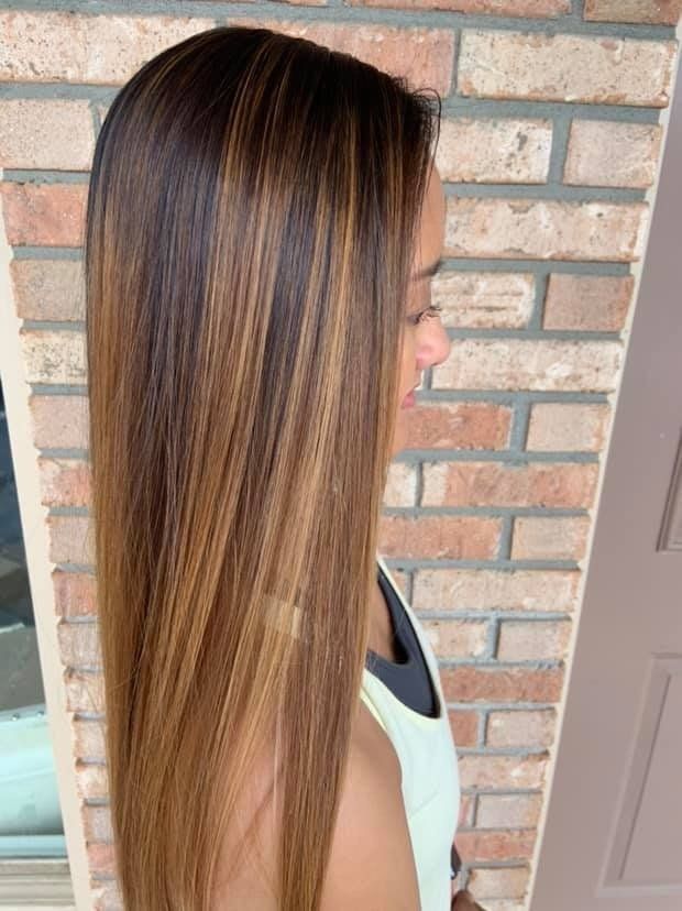 Side view of long straight brown hair with blonde highlights against a brick wall and door.