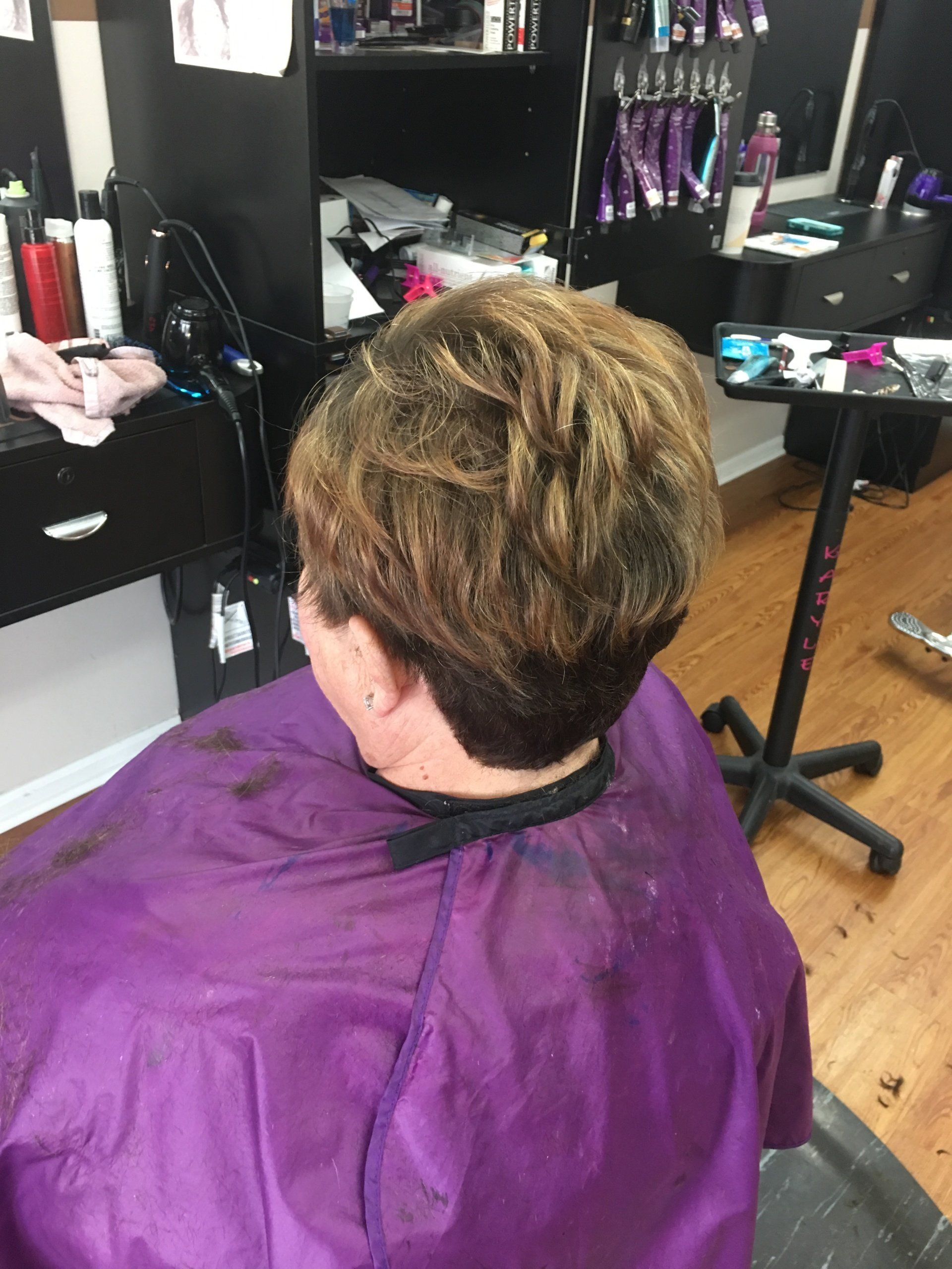 Person seated in a salon chair, wearing a purple cape during a haircut.