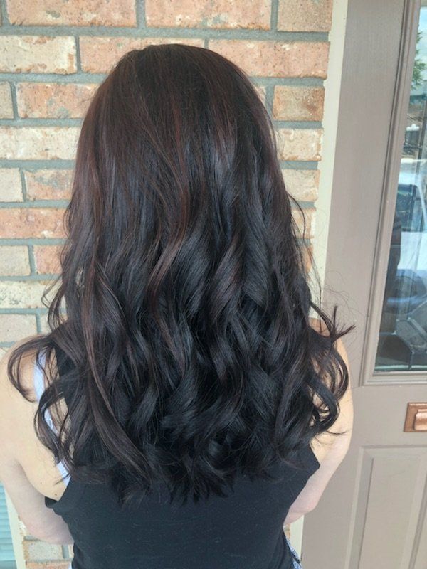 Long dark wavy hair falling to the shoulders against a brick wall and door background