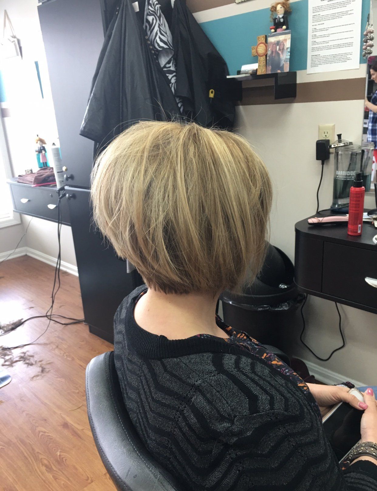 Person with short blonde hair sitting in a salon chair, viewed from behind.