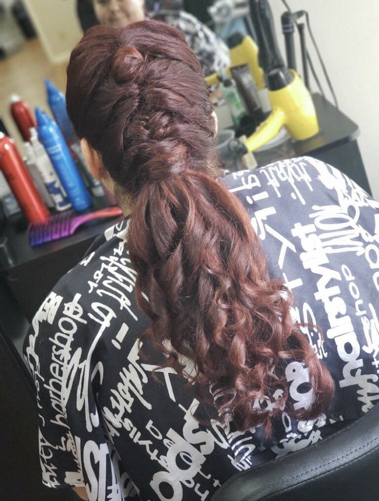 Braided auburn hair styled in a ponytail, seen from behind in a salon chair with tools in the background