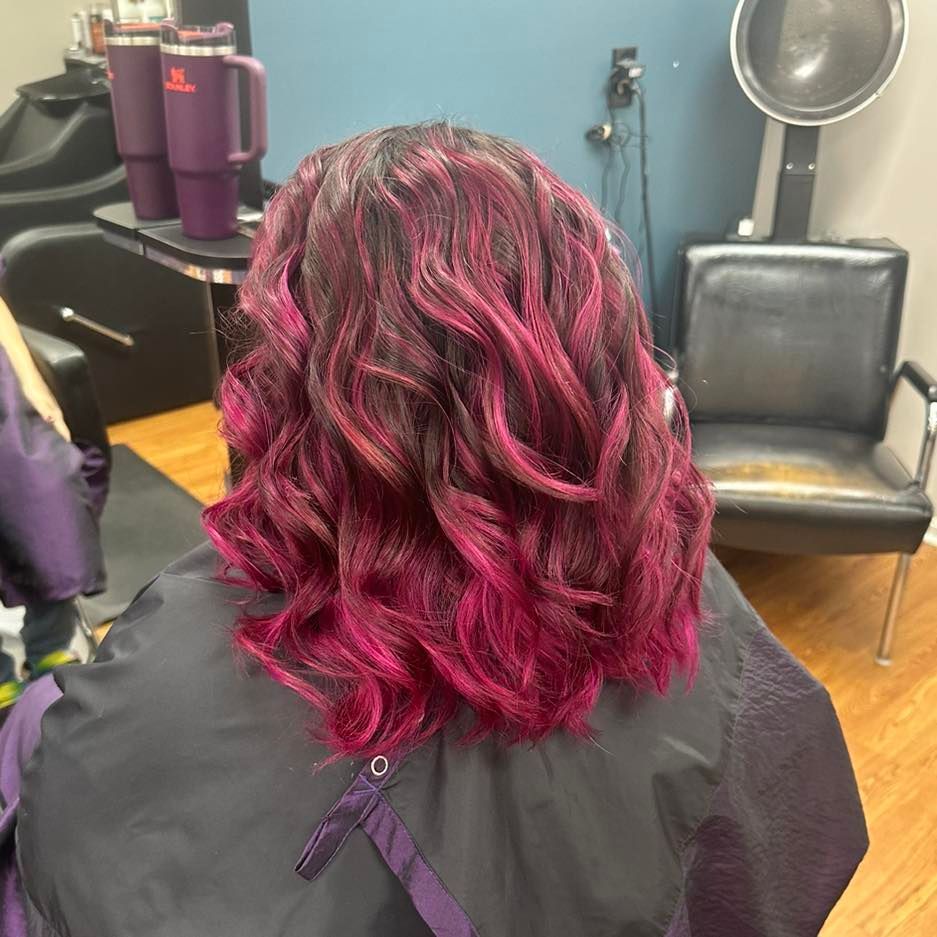 Salon chair view of shoulder-length wavy hair dyed magenta and dark red-black
