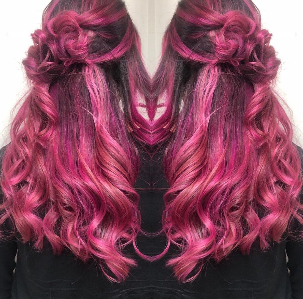 Pink wavy hair styled in two half-up buns against a black background